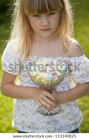 Cute little girl holding a glass bowl full of pastel colored marshmallow candy