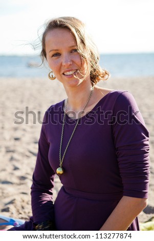 Portrait of a happy, smiling woman sitting on the sand at the beach during summer.