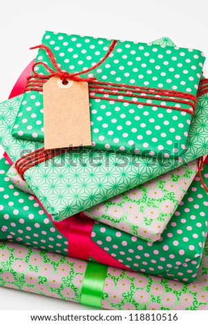 Close up of wrapped gifts with red ribbon and plain cardboard tag on white background