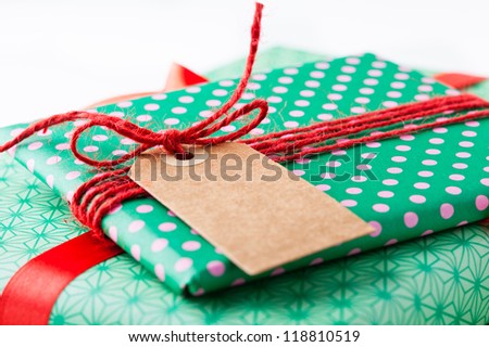 Close up of wrapped gifts with red ribbon and plain cardboard tag on white background
