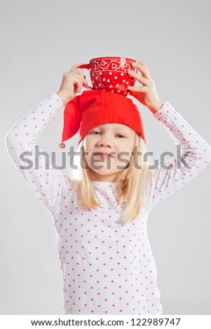 Studio portrait of smiling young girl wearing red Christmas elf hat holding big red cup on head