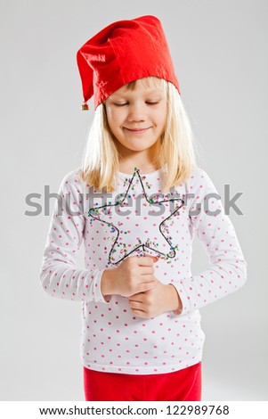Studio portrait of smiling young girl wearing red Christmas elf hat and holding star decoration