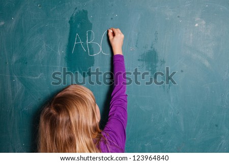 Young girl writing letters of the alphabet on chalkboard with chalk