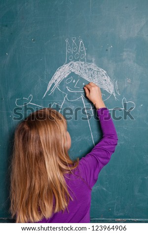 Young girl drawing an image of a princess with crown on chalkboard