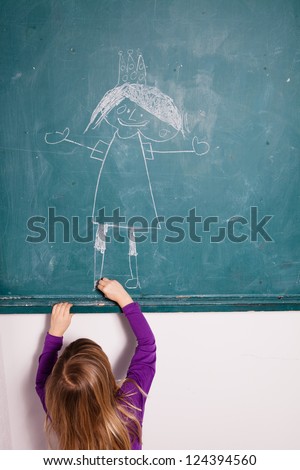 Studio portrait of young girl in classroom drawing image of princess with crown on a chalkboard