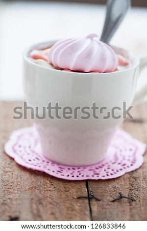 Closeup of cup of hot chocolate with pink meringue and spoon resting on small pink table mat on wooden table