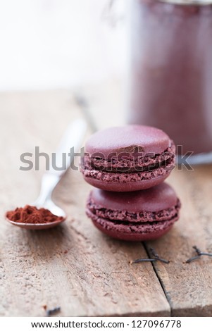 Closeup of two macaroons on wooden table with glass jar of cocoa powder and spoon