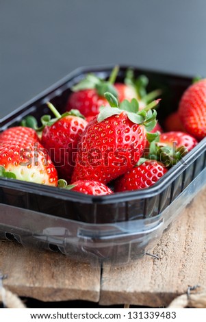 Fresh whole strawberries in plastic packing tray on wooden surface