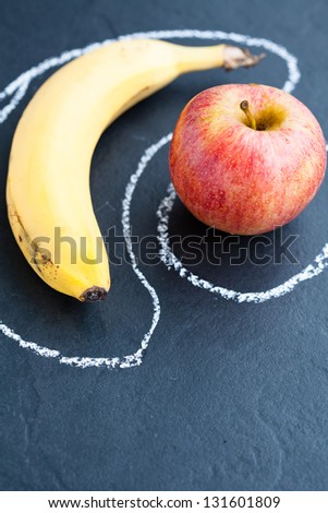 Closeup of apple and banana inside chalk outlines on dark background