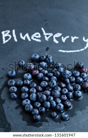 Fresh blueberries and word blueberry written in chalk on dark background