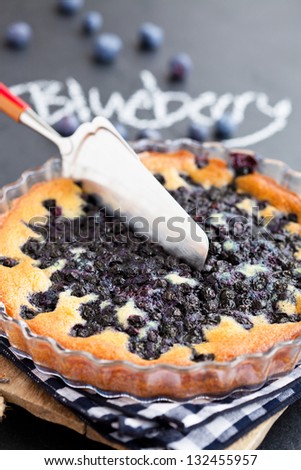 Closeup of lueberry pie in glass dish and server with word blueberry written in chalk on dark background