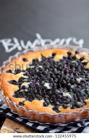 Closeup of blueberry pie in glass dish with word blueberry written in chalk on dark background