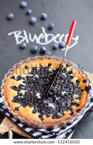 Blueberry pie in glass dish and server with word blueberry written in chalk on dark background