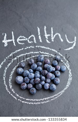 Closeup of healthy fresh blueberries inside circle drawn with chalk and word healthy written on dark background