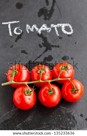 Closeup of fresh red tomatoes with word tomato written in chalk on dark background