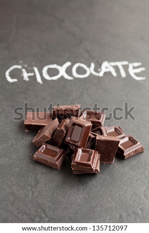 Closeup of pile of chocolate squares with word chocolate written in chalk on dark background