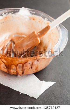 Closeup of messy empty glass bowl of chocolate cake mix with plastic spatula on dark background