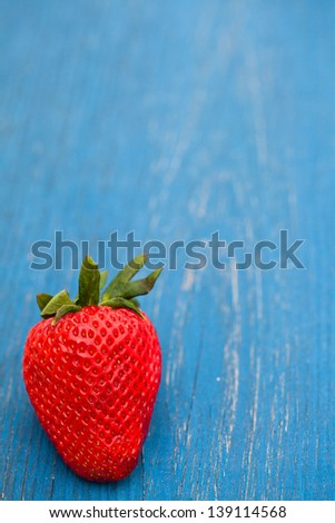 Closeup of one large fresh strawberry against light blue wooden background