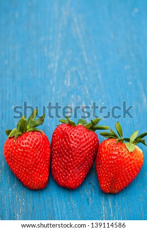 Closeup of three large fresh strawberries in row against light blue wooden background