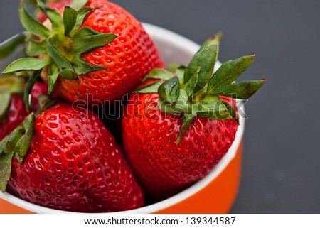 Closeup of large fresh strawberries in orange bowl against dark background