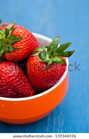 Closeup of large fresh strawberries in orange bowl against light blue background