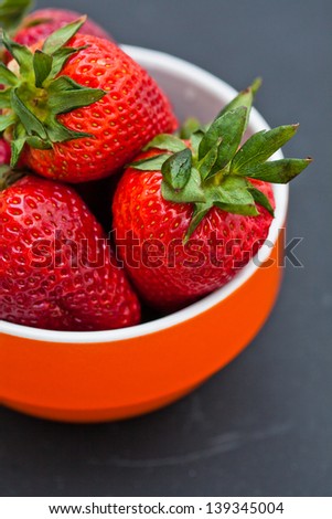 Closeup of large fresh strawberries in orange bowl against dark background