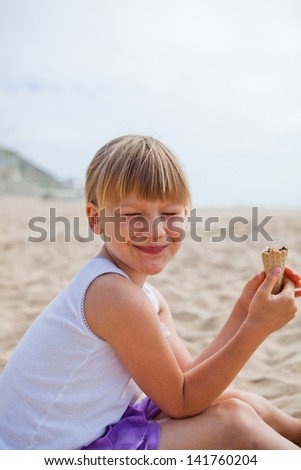 Young happy smiling girl sitting on beach with half eaten ice cream cone