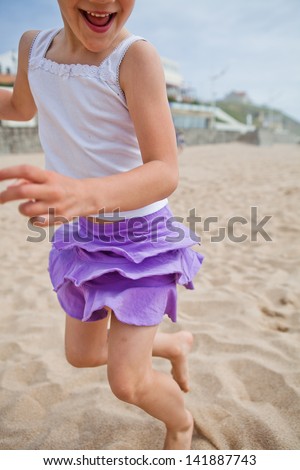 Closeup of happy barefoot young girl in purple skirt and white top playing on beach