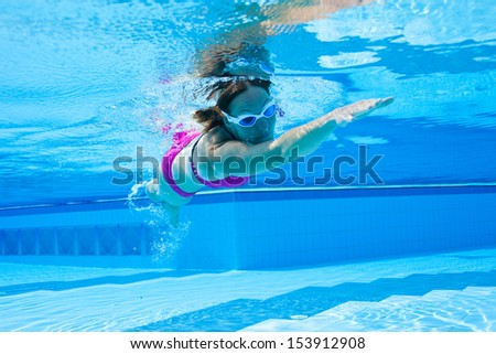 Underwater view of female with violet swimsuit and white goggles swimming in pool