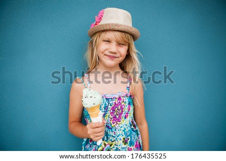 Cute smiling young girl holding ice cream cone outside against blue wall background
