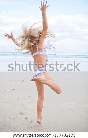 Young cute girl in swimming suit having fun at the beach by jumping in air