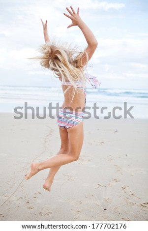 Young cute girl in swimming suit having fun at the beach by jumping in air
