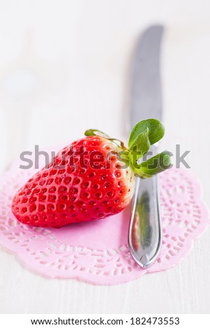 Closeup of fresh whole strawberry and silver metal knife resting on decorative pink mat