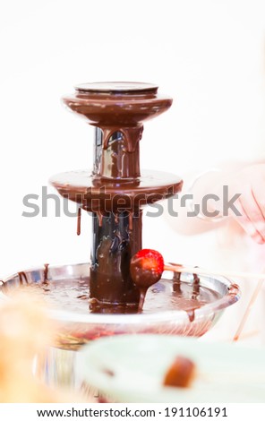 Closeup of chocolate fondue fountain with one strawberry on stick