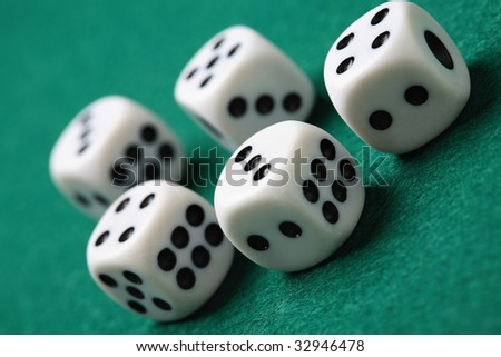 A close-up of five white gambling or playing die with black markings on a green felt cloth surface.
