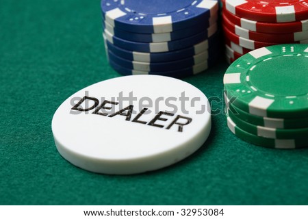 A close-up of a dealer button in front of poker chips on a green felt cloth playing surface.