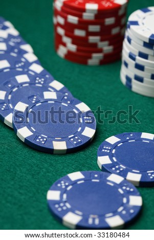 A close-up of poker chips spread out over a green surface with stacks of poker chips in the background.