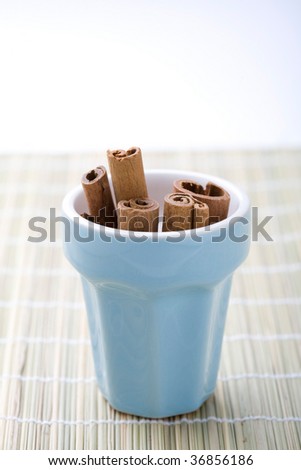 A close-up of dry whole cinnamon sticks in a light blue cup resting on a table mat.