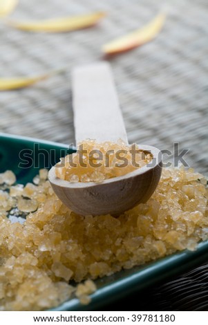 A close-up of yellow colored bath salt crystals in a wooden spoon and turquoise colored dish used in a health and beauty spa.