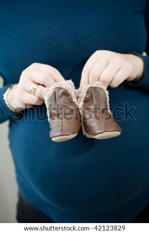 Pregnant mother holding cute little leather baby booties in front of her tummy