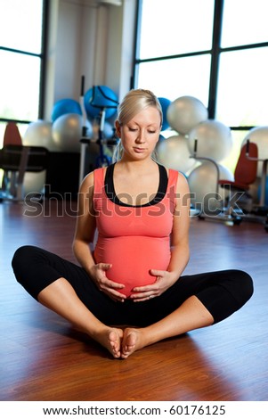 A pregnant woman sitting on the floor of a gym relaxing and holding her belly.