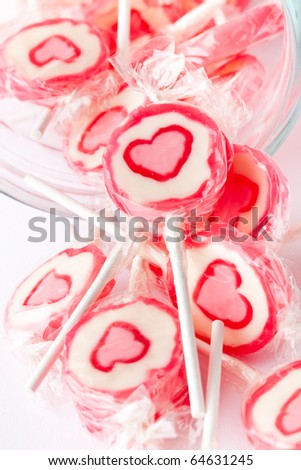 Close-up of pink lollipops with heart in the middle. On white in a glass jar.