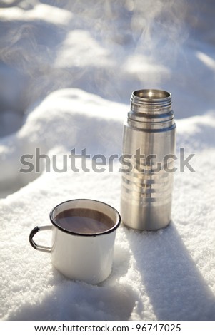Mug and thermos of hot chocolate on a cold winter day in snow