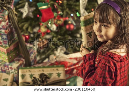 well hold on, what\'s this? / little girl checking a gift / to see what\'s inside