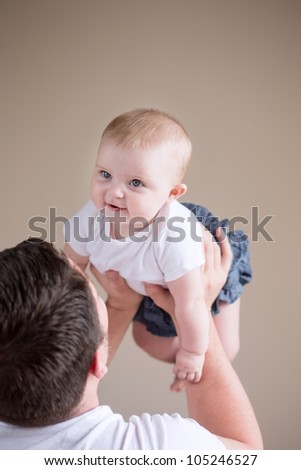 Studio Shot of Loving Father Lifting Smiling Baby Above Head