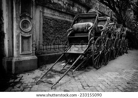 Black and white image of traditional hand pulled Indian rickshaws parked together in front of a old building in Kolkata