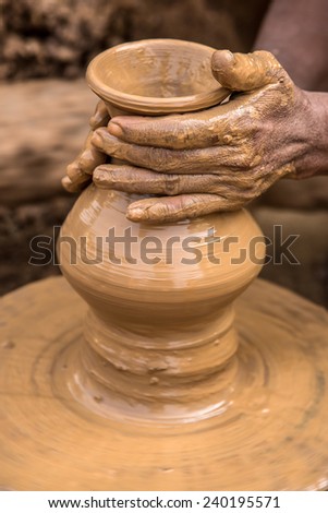 Hands of a clay artisan working to make a flower vase out of soft clay on a rotating cart wheel