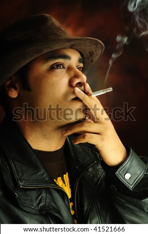 Portrait of a young man in dramatic lighting, wearing hat smoking a cigarette with thoughtful expression