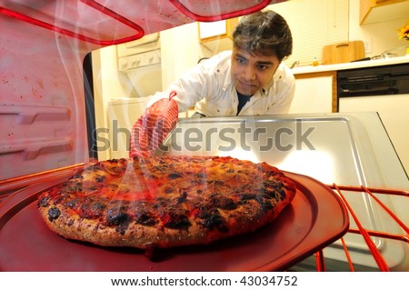 Young man taking out delicious hot pizza cooked at home in the oven