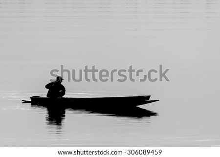 Monotone of Silhouette of a man on paddling boat is fishing on the river